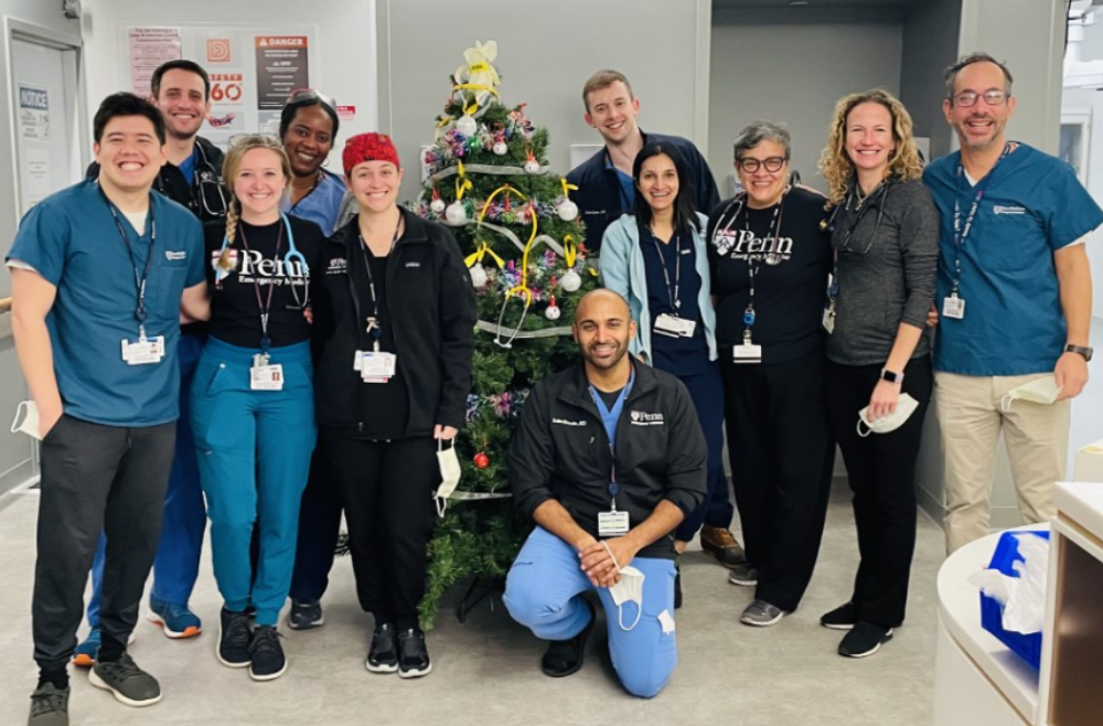 Mira Mamtani, standing on the right side of a Christmas tree, poses with ten residents and physicians in the Emergency Department